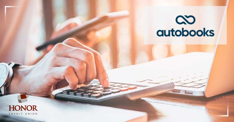 simplify your business accounting with the help of honor credit union and autobooks; hand holding phone while other hand types on calculator