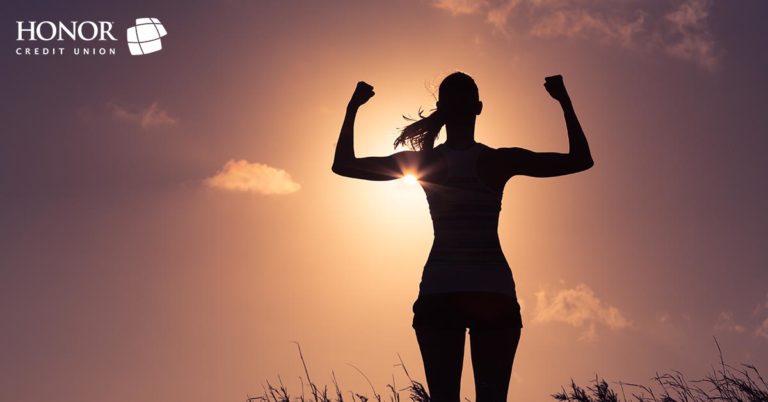 honor credit union can help you create a plan to save money; woman flexing her muscles in a sunset