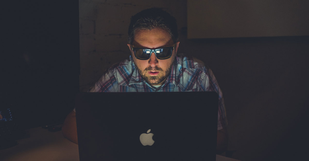 there are practical ways to protect your online identity and profiles; photo of man wearing sunglasses in dark room typing on computer