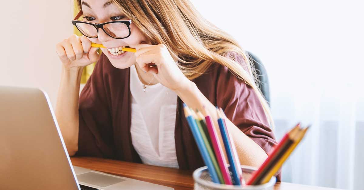 student loan debt is frustrating for many college graduates; photo of woman biting a pencil looking at a computer screen