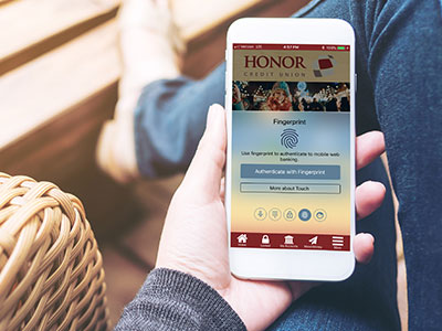 logging in to the honor app is simple with biometric authentication; photo of a hand holding a mobile phone with the honor credit union mobile app open