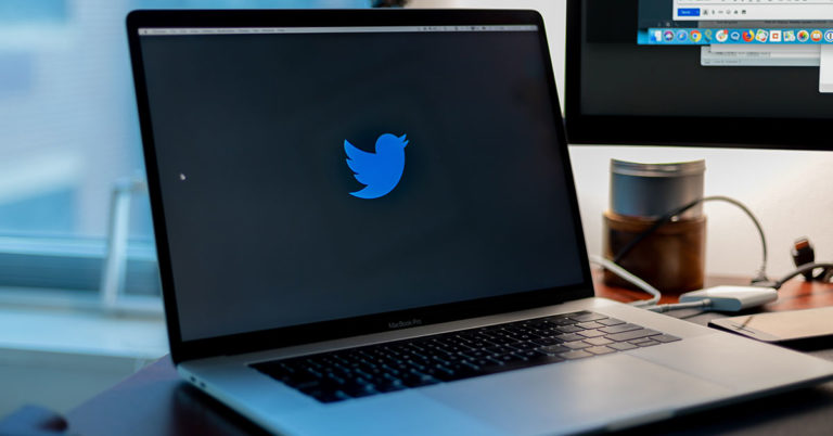 photo of a laptop resting on a desk displaying the Twitter logo