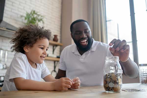 photo of a father and daughter putting loose change in a glass jar at a table
